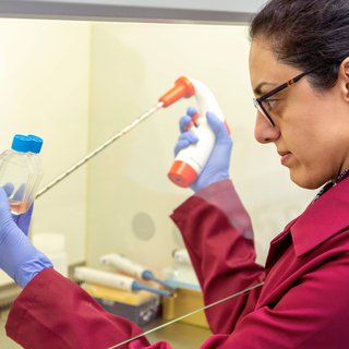 A female blood cancer researcher stands in a lab using a large pipette whilst looking at a sample in a small bottles.