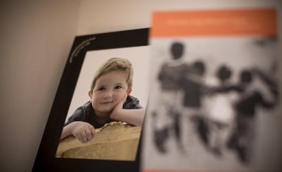 A framed photo of Hugo, a young blonde boy in remission from childhood leukaemia, leaning on a log, looking at the camera.
