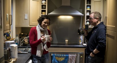 Paul, living with CML, has a cup of tea with his wife laughing wife in the kitchen.