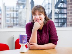 Former Blood Cancer UK Chief Executive, Gemma Peters, sits smiling at a table with a collection pot next to her.