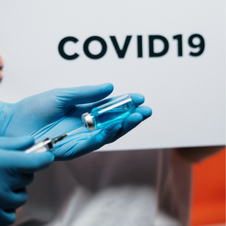 A close up of someone's hands with blue gloves on - they are squeezing a syringe into a vile.