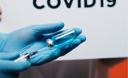 A close up of someone's hands with blue gloves on - they are squeezing a syringe into a vile.