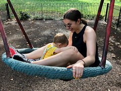 A mother and child playing on a swing in the playground on a sunny day, laughing and having fun.