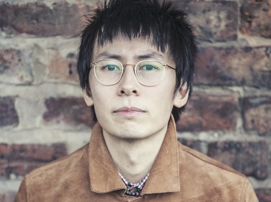 Head and shoulders shot of David, standing against a brick wall.