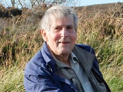 A middle aged man, smiling slightly at the camera, sitting in a green field.