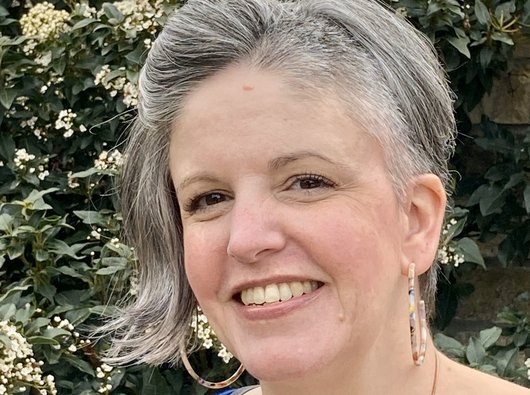 Esther, who has been living with ET since 2018, smiling in front of some flowering shrubs