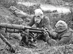 World War One image of man with rudimentary gas mask on preparing a machine gun on the battlefield.