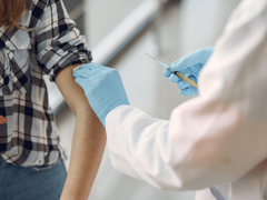 Close up of a doctor with blue gloves who has just injected a blood cancer patient in a checked shirt in their upper arm.