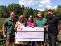 People smiling holding a check in front of trees
