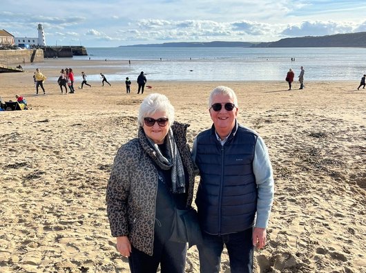 Jacqui walking with her partner on the beach, on a sunny autumn day.