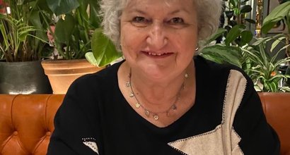 Jacqui, diagnosed with PV, seated at a restaurant table with plants behind.