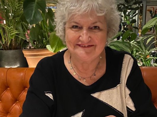 Jacqui, diagnosed with PV, seated at a restaurant table with plants behind.