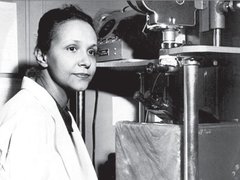 A scientist - Jane C Wright, surgeon and early chemo researcher, poses next to a microscope in a black and white photograph.