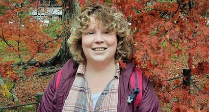 Katherine on holiday in Japan, smiling in front of a colourful maple tree.