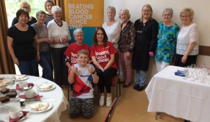 Johanna, who is affected by blood cancer, sat with friends in front of a Bloodwise banner.