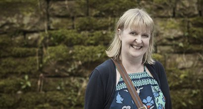 An image of Kate, who was diagnosed with non-Hodgkin's lymphoma, smiling and standing to the left of a wall.