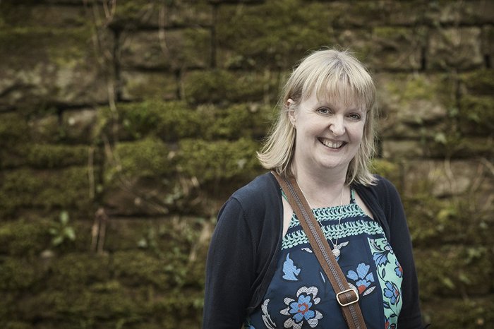 An image of Kate, who was diagnosed with non-Hodgkin's lymphoma, smiling and standing to the left of a wall.