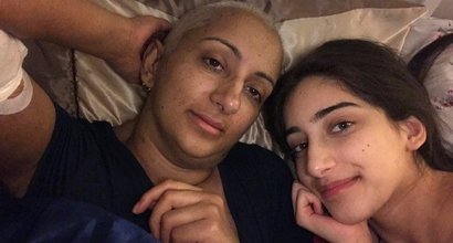 Kal (on the left) with her daughter. They are lying on a bed together, looking up at the camera.