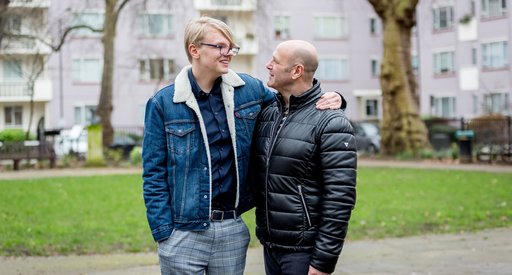 A male couple share a tender moment in a housing estate garden.