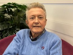 Louis Walsh in blue jumper sitting wearing pin badge