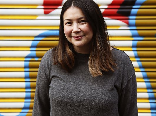 A headshot of Louise Lai, trustee of Blood Cancer UK, with a brightly coloured painted wall in the background.