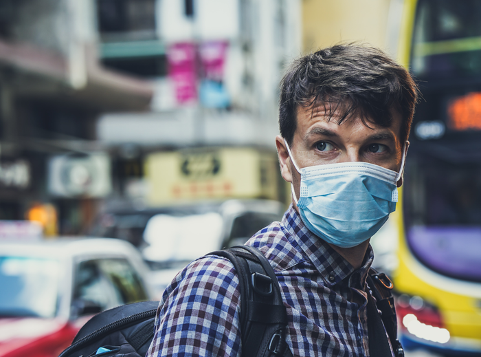 A close up image of a man wearing a blue medical mask, looking away from the camera.