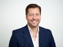 Matthew Wilson, a member of the Board, smiling against a plan white background.