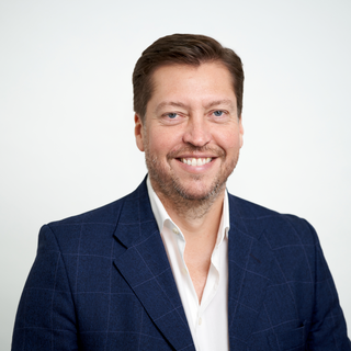 Matthew Wilson, a member of the Board, smiling against a plan white background.