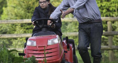 A man, who has chronic lymphocytic leukaemia, standing next to a girl on a lawnmower in a garden.
