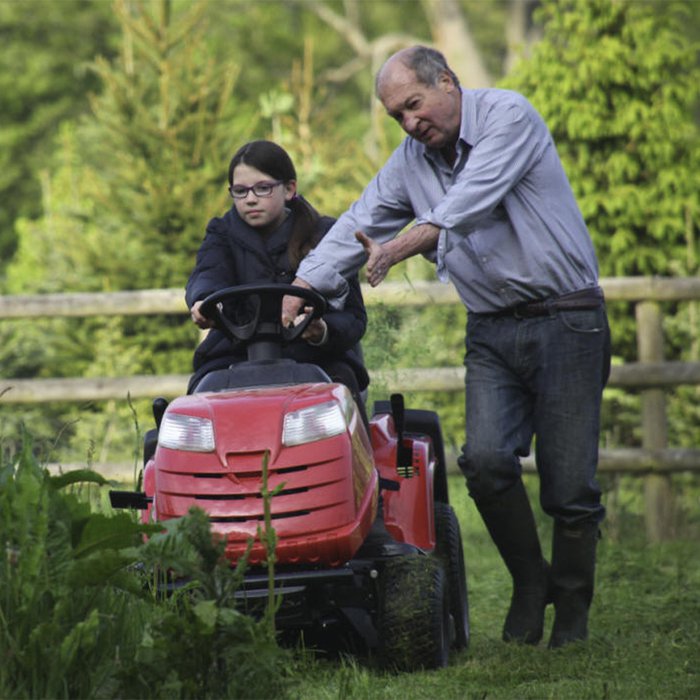 A man, who has chronic lymphocytic leukaemia, standing next to a girl on a lawnmower in a garden.