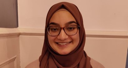 Nabeela, a young woman wearing glasses and a headscarf, smiling at the camera