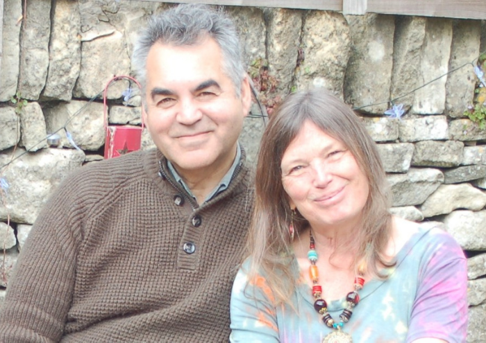 Nicky, a woman who lives with chronic lymphocytic leukaemia (CLL) and participated in a clinical trial, sits next to a man in front of a stone wall.