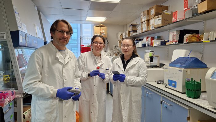 Dr Feldhahn in the stood in the lab with two members of his lab team, wearing white lab coats.