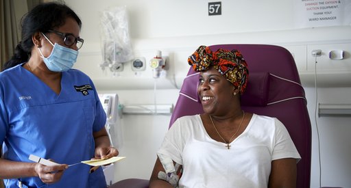 A nurse stands next to a patient sitting on a hospital bed in a treatment room.