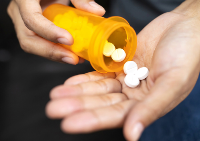 Close-up of pills being emptied from a plastic container into a hand.