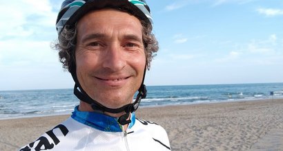 Quentin, who lives with acute myeloid leukaemia (AML), stands on a sandy beach wearing cycling clothes and a helmet.