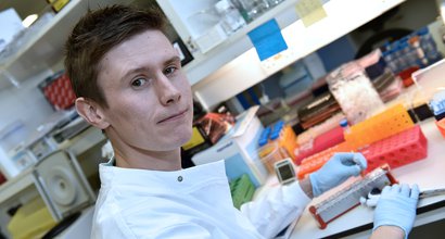 Dan Coleman, from the University of Birmingham, stands in a laboratory holding a test tube.