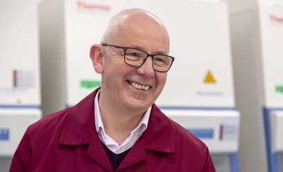 Professor Chris Bunce stands in a red lab coat in a laboratory.