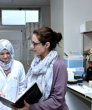 Three researchers (Yao Jiang, Jennifer Butler, and Farhat Khanim) looking at a book together in a University of Birmingham research lab.