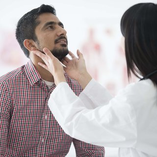 Doctor examining patient's throat by feeling for swollen lymph nodes in examination room.