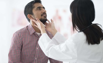 Doctor examining patient's throat by feeling for swollen lymph nodes in examination room.