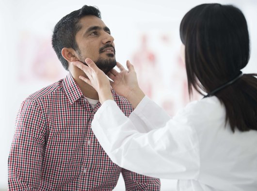 Doctor examining patient's throat by feeling for swollen lymph nodes in examination room.