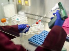 A close up of a researcher's hands in a lab, holding a pipette and test tubes.