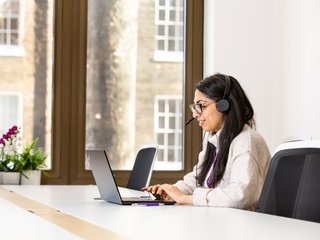 Tanya Kumar, a support services member of staff, taking a call on the helpline in the office. She is wearing headphones and looking at her computer.