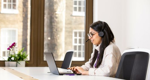Tanya Kumar, a support services member of staff, taking a call on the helpline in the office. She is wearing headphones and looking at her computer.
