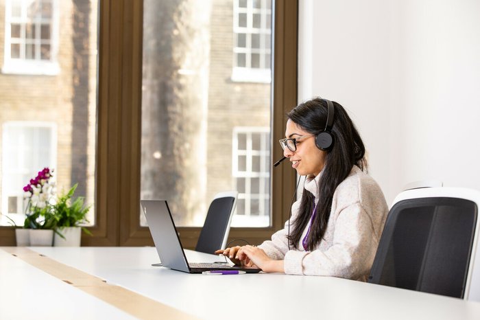 Tanya Kumar, a support services member of staff, taking a call on the helpline in the office. She is wearing headphones and looking at her computer.