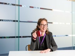 Blood Cancer UK's CEO, Helen Rowntree, holding a Blood Cancer UK coffee mug in the office and smiling.
