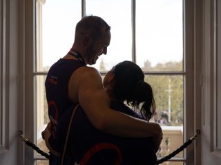 Man and woman hugging, standing by a window.