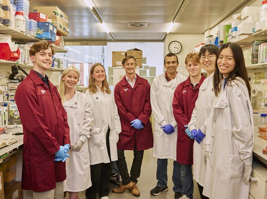 A group of Blood Cancer UK researchers all standing together in a lab, wearing their lab coats and smiling.