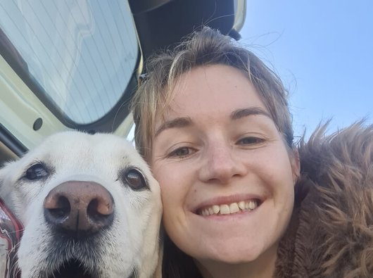 A young woman (Jade) cuddled up to a dog. She's smiling happily.